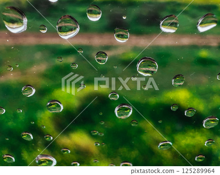 Extremely close up macro drops of water on a wet glass on natural green background. Raindrops pattern on smooth surface. Rainy day. Abstract wallpaper 125289964