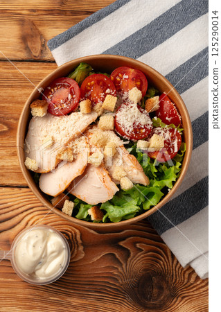 Fresh salad bowl with grilled chicken, tomatoes, croutons, and creamy dressing prepared on rustic wooden table Fresh salad bowl with grilled chicken, tomatoes, croutons, and creamy dressing prepared on rustic wooden table 125290014
