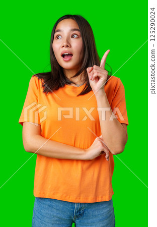 Young woman expressing surprise with one finger raised, wearing an orange shirt against a bright green background Young woman expressing surprise with one finger raised, wearing an orange shirt against a bright green background 125290024