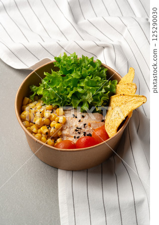 Healthy lunch bowl featuring corn, lettuce, and tortilla chips on a gray table with a striped cloth backdrop Healthy lunch bowl featuring corn, lettuce, and tortilla chips on a gray table with a striped cloth backdrop 125290030