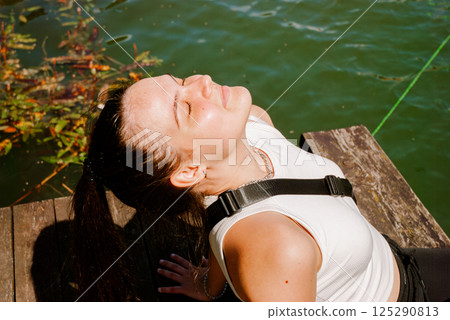 Relaxation by the water, young woman enjoying sunlight on a dock. Weekend concept near the forest and lake Relaxation by the water, young woman enjoying sunlight on a dock. Weekend concept near the forest and lake 125290813