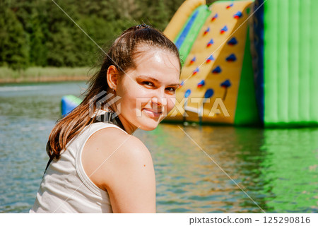 Woman enjoying a summer day by the lake with inflatable water park in background. Weekend concept near the forest and lake 125290816