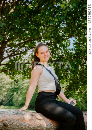 Young woman relaxing on tree log in nature park setting. Weekend concept near the forest and lake 125290818