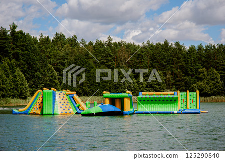 Inflatable obstacle course on lake with forest backdrop for summer fun. Weekend concept near the forest and lake Inflatable obstacle course on lake with forest backdrop for summer fun. Weekend concept near the forest and lake 125290840