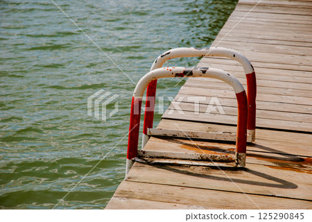 Calm lakeside scene with wooden dock and rusted metal ladder for relaxation and recreation. Weekend concept near the forest and lake Calm lakeside scene with wooden dock and rusted metal ladder for relaxation and recreation. Weekend concept near the forest and lake 125290845
