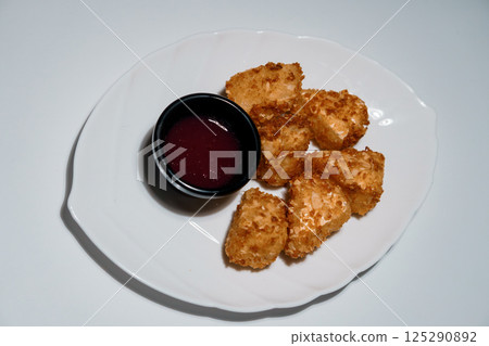 Crispy chicken nuggets with dark red berry sauce served on a white plate, top-down view isolated on white background 125290892