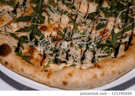 Close-up of a gourmet pizza topped with fresh arugula, grated parmesan cheese and balsamic glaze on a rustic crust 125290899