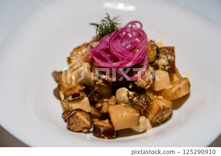 Gourmet dish featuring sausage, mushrooms and potatoes topped with pickled red onions and fresh dill on white plate 125290910
