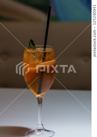 Refreshing orange cocktail in a tall glass with ice cubes and mint garnish, presented on white surface with blurred background Refreshing orange cocktail in a tall glass with ice cubes and mint garnish, presented on white surface with blurred background 125290941