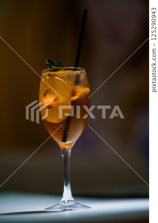 Refreshing orange cocktail in a wine glass with ice, garnished with mint and citrus twist served on table 125290943