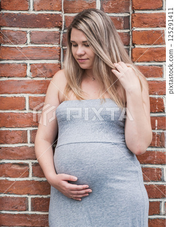 Beautiful pregnant woman posing against a brick wall while touching her belly in natural light Beautiful pregnant woman posing against a brick wall while touching her belly in natural light 125291411