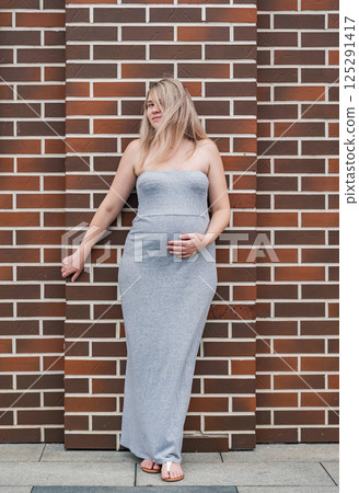 Beautiful pregnant woman posing against a brick wall while touching her belly in natural light Beautiful pregnant woman posing against a brick wall while touching her belly in natural light 125291417