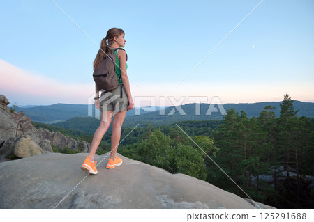 Young woman hiking alone on mountain footpath. Female hiker enjoying view of evening nature on wilderness trail. Active way of life concept Young woman hiking alone on mountain footpath. Female hiker enjoying view of evening nature on wilderness trail. Active way of life concept 125291688