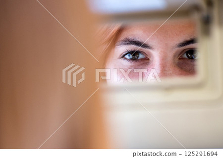 Young woman driver checking rear view mirror looking backwards while driving a car. 125291694