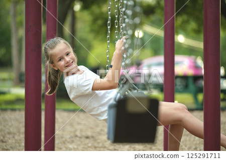 Young pretty smiling teenage girl playing alone on swings on summer playground 125291711