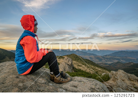 Young child boy hiker sitting in mountains enjoying view of amazing mountain landscape. 125291723