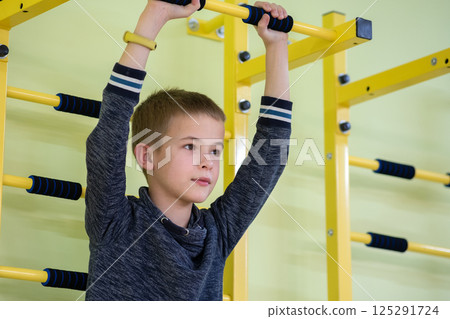 Young child boy exercising on a wall ladder bar inside sports gym room in a school. Young child boy exercising on a wall ladder bar inside sports gym room in a school. 125291724