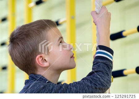 Young child boy exercising on a wall ladder bar inside sports gym room in a school. 125291725