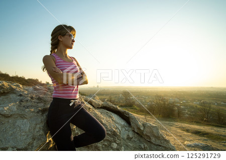 Woman hiker leaning on a big rock enjoying warm summer day. Young female climber resting during sports activity in nature. Active recreation in nature concept. Woman hiker leaning on a big rock enjoying warm summer day. Young female climber resting during sports activity in nature. Active recreation in nature concept. 125291729