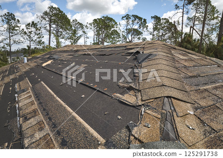 Wind damaged house roof with missing asphalt shingles after hurricane Ian in Florida. Repair of home rooftop concept Wind damaged house roof with missing asphalt shingles after hurricane Ian in Florida. Repair of home rooftop concept 125291738