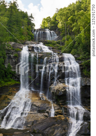 Whitewater Falls in Nantahala National Forest, North Carolina, USA. Beautiful landscape of high waterfall with falling down clear water from rocky boulders between green lush woods Whitewater Falls in Nantahala National Forest, North Carolina, USA. Beautiful landscape of high waterfall with falling down clear water from rocky boulders between green lush woods 125291750