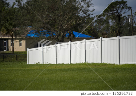 White vinyl picket fence on green lawn surrounding property grounds for backyard protection and privacy White vinyl picket fence on green lawn surrounding property grounds for backyard protection and privacy 125291752