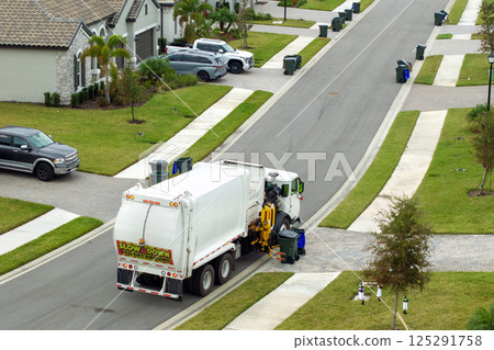 Weekly clean-up. Garbage truck picking up trash bins from the curb in American suburban neighborhood 125291758