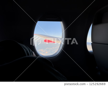 Peaceful moment inside airplane cabin with sleeping passenger near window, soft light illuminating clouds and wing outside, capturing calm travel and quiet relaxation at high altitude 125292669