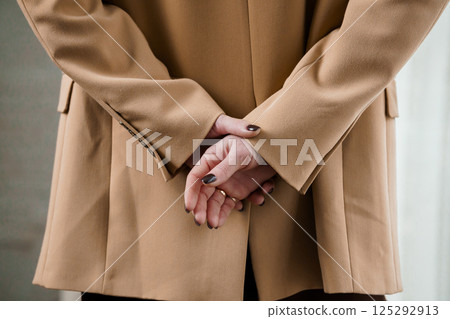 Elegant Woman in Tan Blazer with Hands Behind Back Elegant Woman in Tan Blazer with Hands Behind Back 125292913