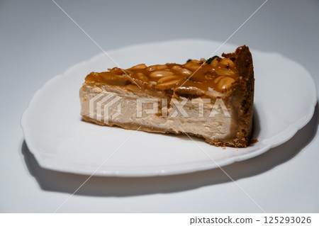 A delicious slice of peanut caramel cheesecake on a white plate, studio shot with soft lighting, showcasing rich textures and inviting dessert presentation 125293026