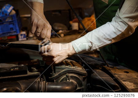 Hands of a mechanic working on a car engine with tools in a garage setting Hands of a mechanic working on a car engine with tools in a garage setting 125293076