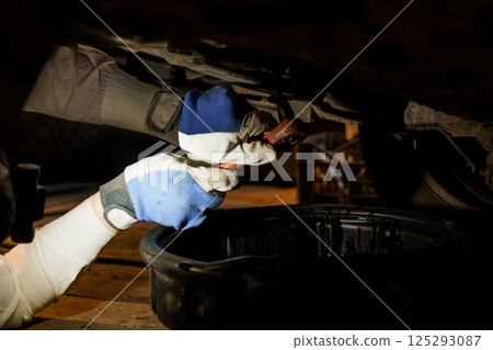 Mechanic Working Under Vehicle with Tools in Dim Lighting 125293087