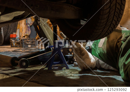 Mechanic Working Underneath Raised Vehicle with Jack Mechanic Working Underneath Raised Vehicle with Jack 125293092
