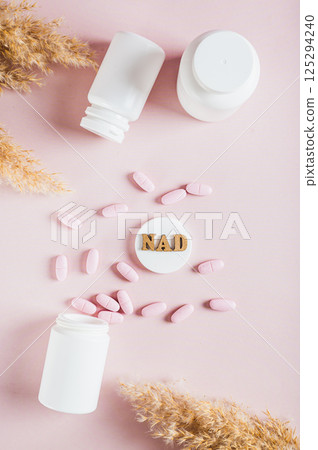 NAD+ molecule in pills for anti-aging and biohacking on pink top and vertical view 125294240