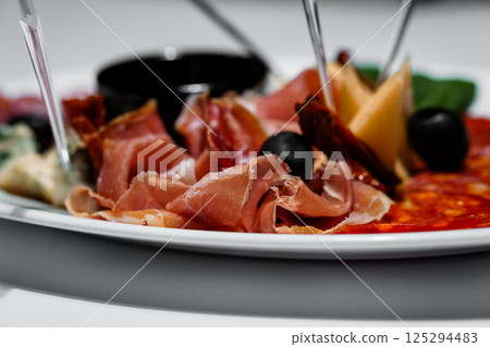 Delicious close-up of a charcuterie board with cured meats, olives, cheese and spicy salami served on white plate Delicious close-up of a charcuterie board with cured meats, olives, cheese and spicy salami served on white plate 125294483