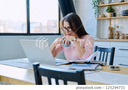 Middle aged woman working with laptop sitting at table at home 125294731