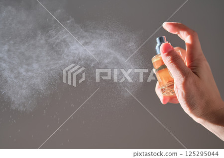 The hand sprays perfume from a transparent rounded bottle. 125295044