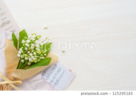 Natural lily of the valley bouquet and sheet music | Wood grain background 125295183