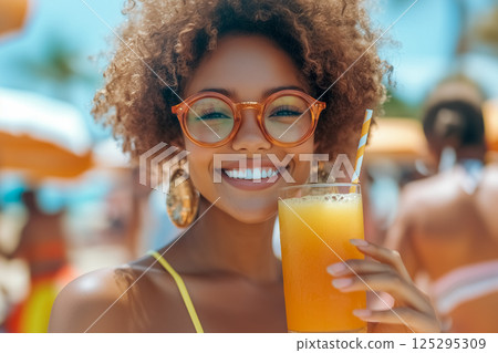 Smiling african american girl in round glasses enjoys refreshing orange juice on sunny beach day in tropical paradise with colorful umbrellas 125295309