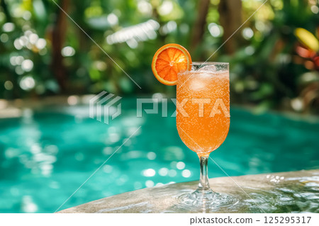Beautiful orange cocktail served by a tranquil poolside oasis surrounded by lush tropical greenery in a serene setting 125295317