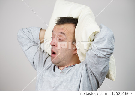 Man sleepy tired with pillow yawning on grey Man sleepy tired with pillow yawning on grey 125295669