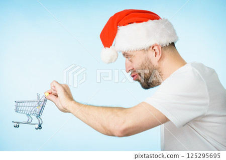 Man in santa hat holds empty shopping cart Man in santa hat holds empty shopping cart 125295695