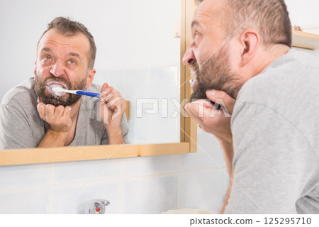 Bored guy brushing his teeth in bathroom Bored guy brushing his teeth in bathroom 125295710
