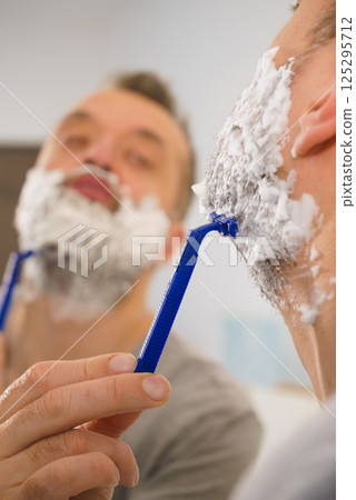 Guy shaving his beard in bathroom Guy shaving his beard in bathroom 125295712