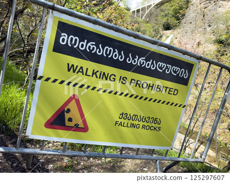 Multilingual warning sign near waterfall in Georgia prohibits walking due to rockfall danger in mountainous area. The danger of falling rocks from mountains in Georgia during nature walks Multilingual warning sign near waterfall in Georgia prohibits walking due to rockfall danger in mountainous area. The danger of falling rocks from mountains in Georgia during nature walks 125297607