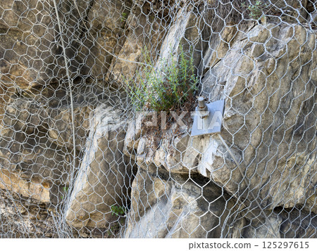 Closeup of rockfall protection mesh and anchored support system on steep rocky slope used for mountain stabilization and erosion prevention in engineering safety solution 125297615