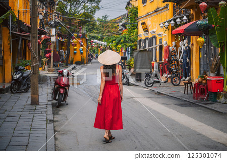 back of a young female tourist in a traditional Vietnamese hat and red dress on the street in old town in Hoi An city in Vietnam in Asia back of a young female tourist in a traditional Vietnamese hat and red dress on the street in old town in Hoi An city in Vietnam in Asia 125301074