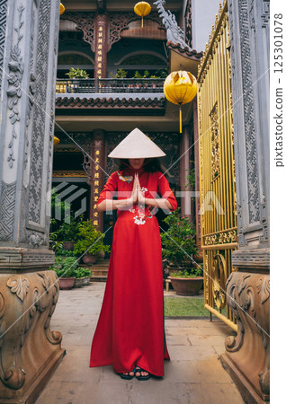female traveler tourist in Vietnamese hat prays at a Buddhist temple on a pagoda in Hoi An in Vietnam in Asia 125301078