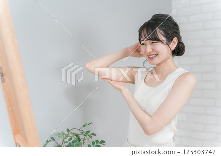 A smiling Asian woman doing a body check in the mirror (upper arm) A smiling Asian woman doing a body check in the mirror (upper arm) 125303742