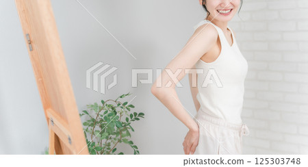 Smiling Asian woman checking her buttocks in the mirror (hip up) 125303748